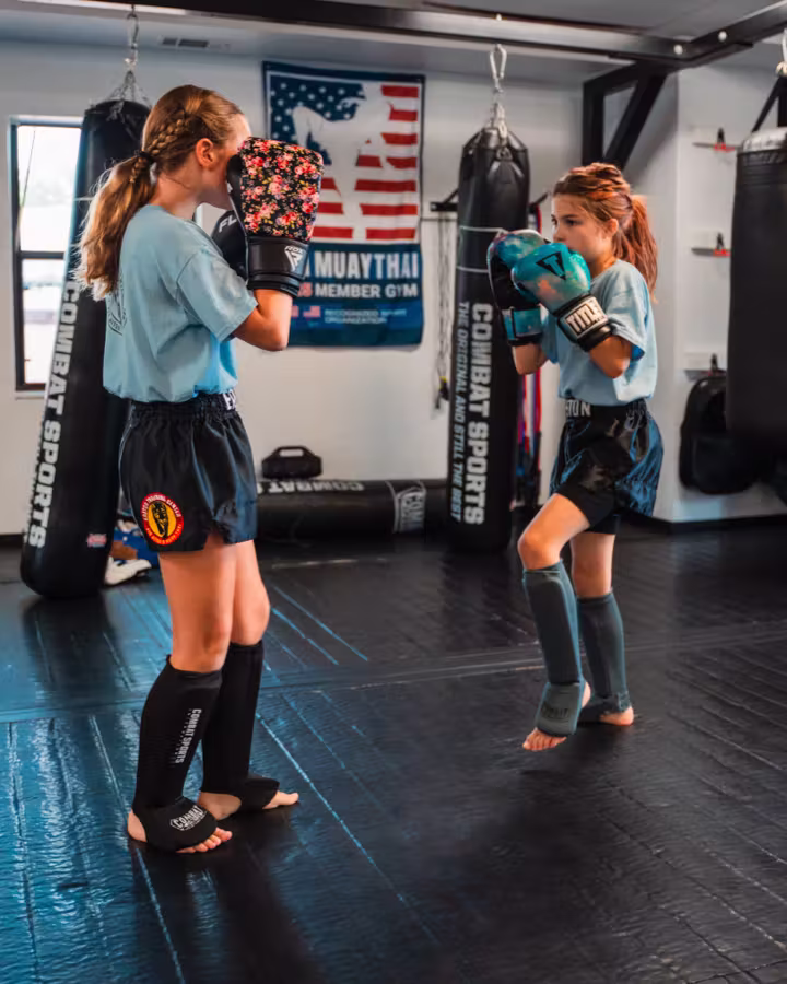 Two girls in a kids Muay Thai class practising their guard beside the heavy bags.