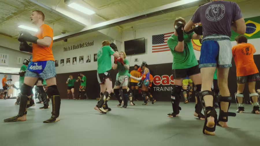 An adult Muay Thai class working in pairs in gloves and shin guards.