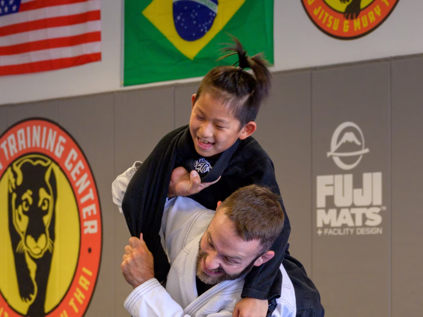 Coach on his knees as a girl climbs onto his back in a Kids Jiu Jitsu drill