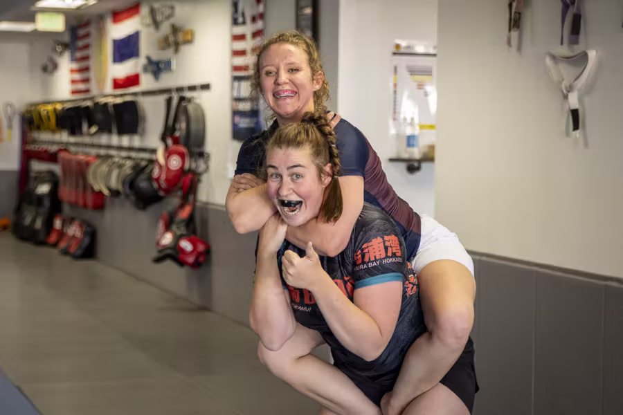 Two training partners at Easton Denver, one taking the other’s back, grinning at the camera