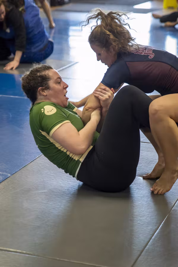 Two women rolling no-gi, one working an armbar from guard