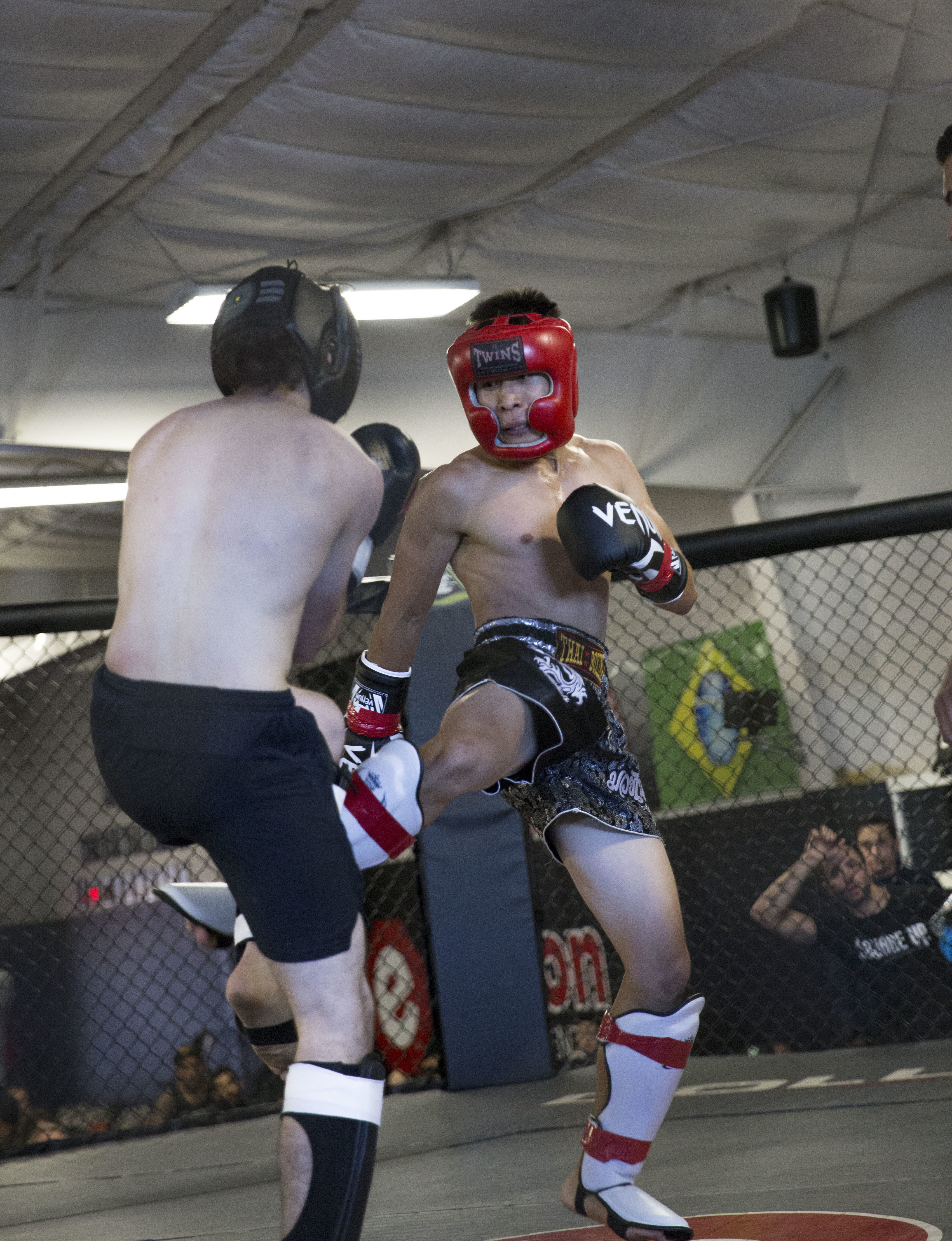One man kicks another in a Muay Thai fight in the MMA cage at Easton Training Center Denver.