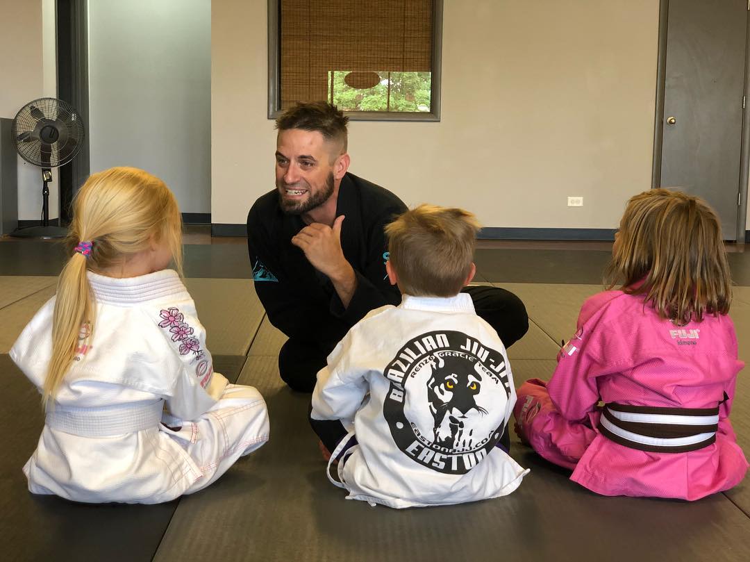 A coach sits with three Little Tigers BJJ students giving the daily Easton Mat Chat