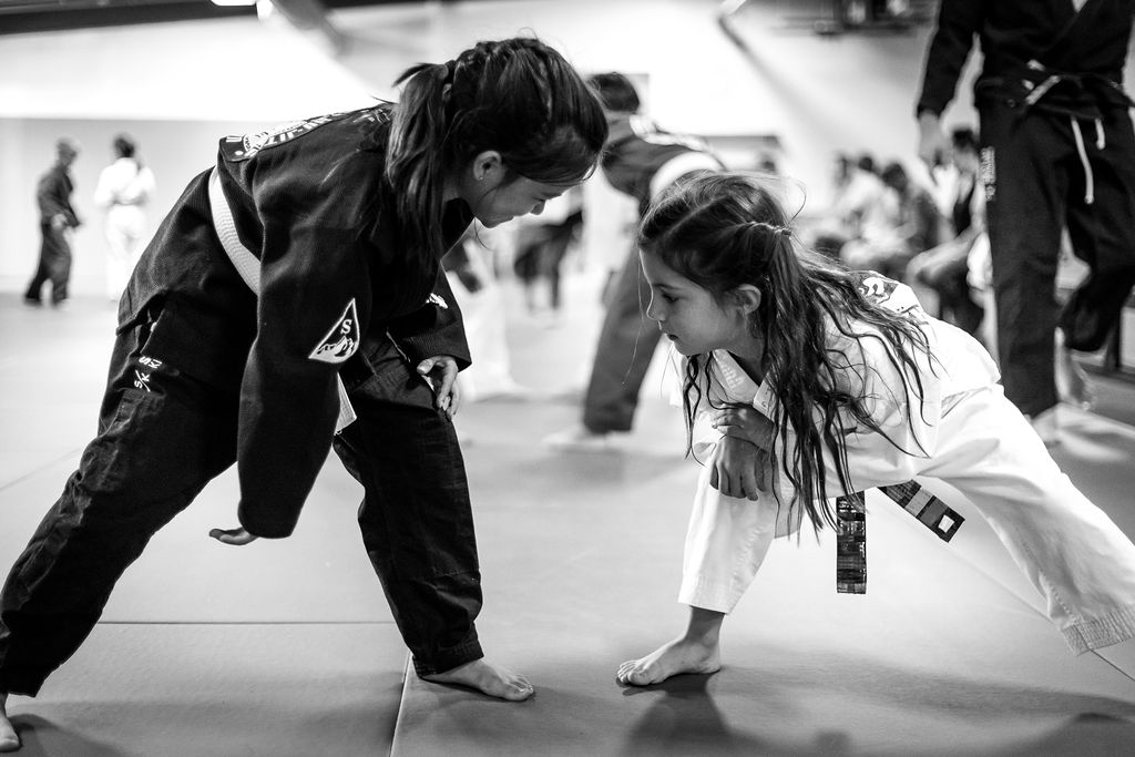 two young girls wearing Brazilian Jiu Jitsu kimonos face off, as one prepares to shoot for a takedown