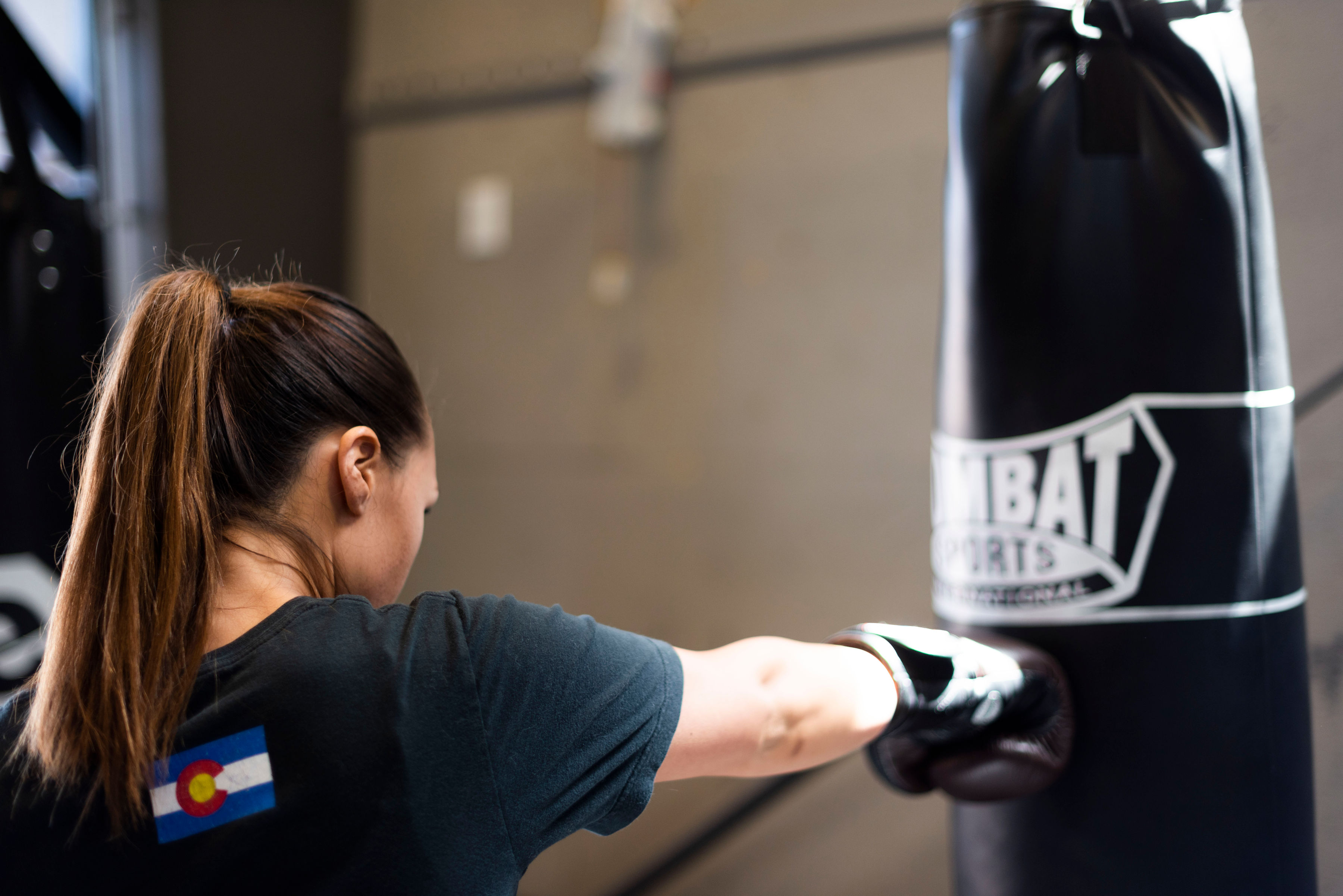 a woman wearing boxing gloves punches a heavy bag with a right cross
