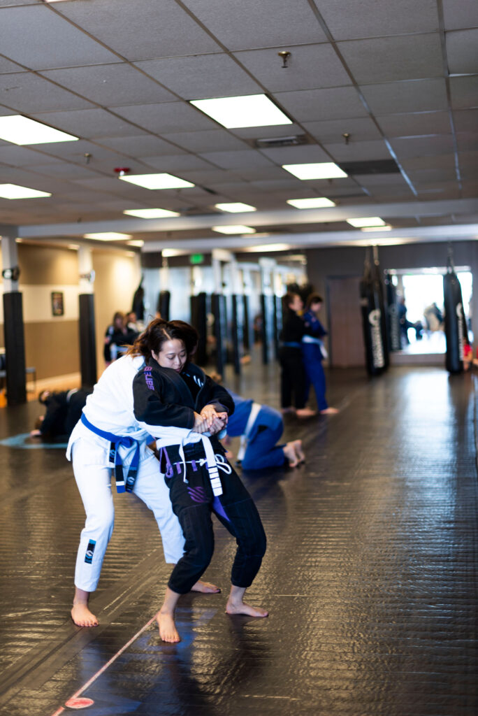 two women wearing brazilian jiu jitsu uniforms practice an escape