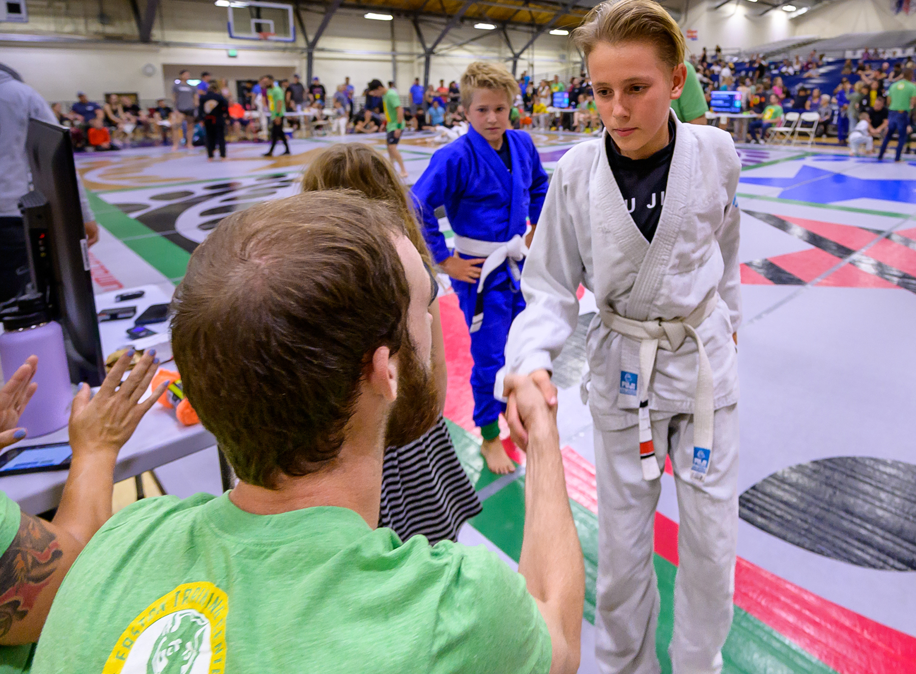 An image of a boy shaking his opponent's coach's hand after their match during a kids jiu-jitsu competition at Easton.