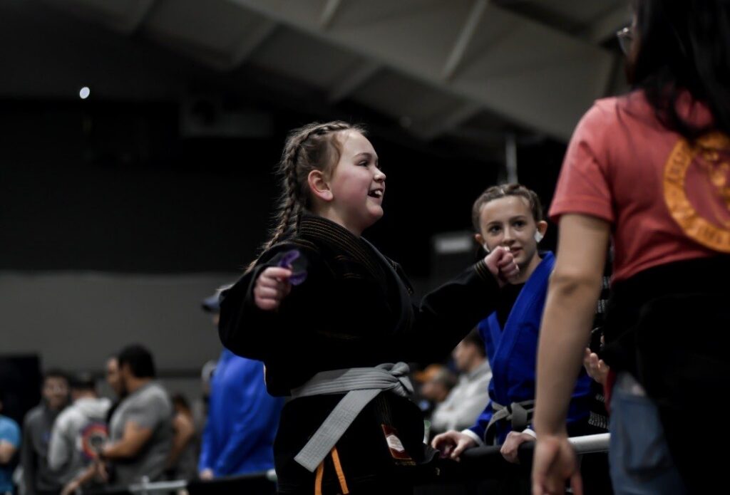 a girl in a black jiu jitsu gi with a gray belt smiles at a tourament