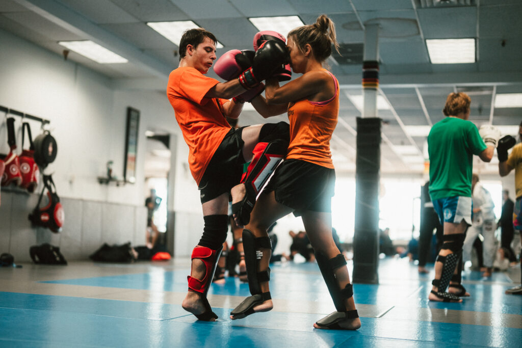 a man and a woman in shin guards and muay thai gloves. The man knees the woman in the stomach. Confidence