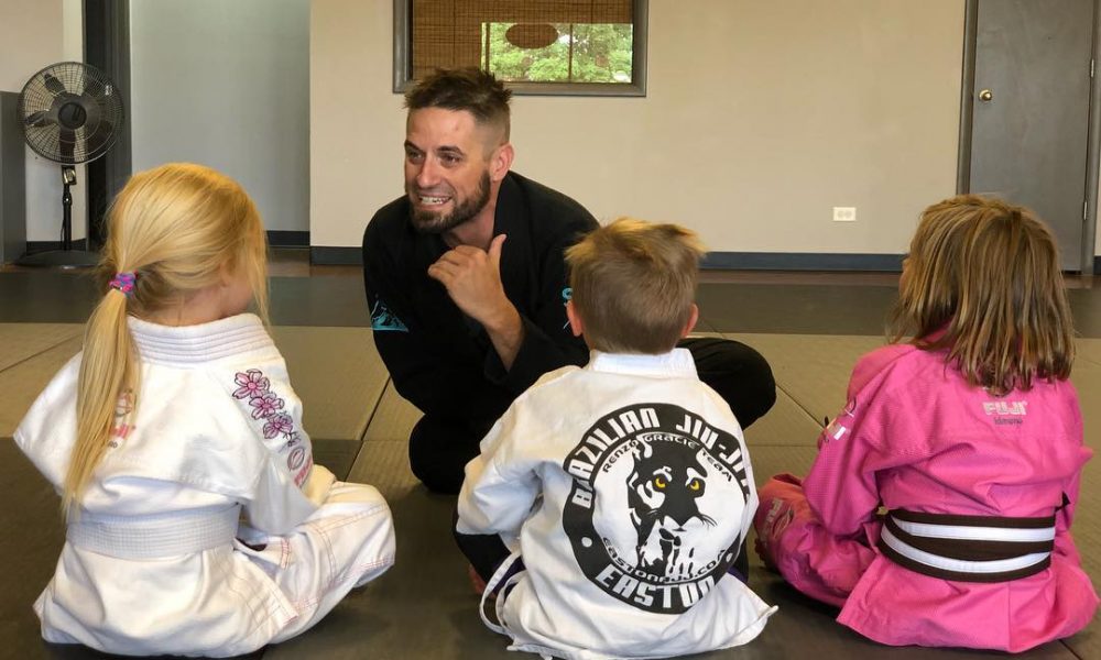 A coach sits with three Little Tigers BJJ students giving the daily Easton Mat Chat