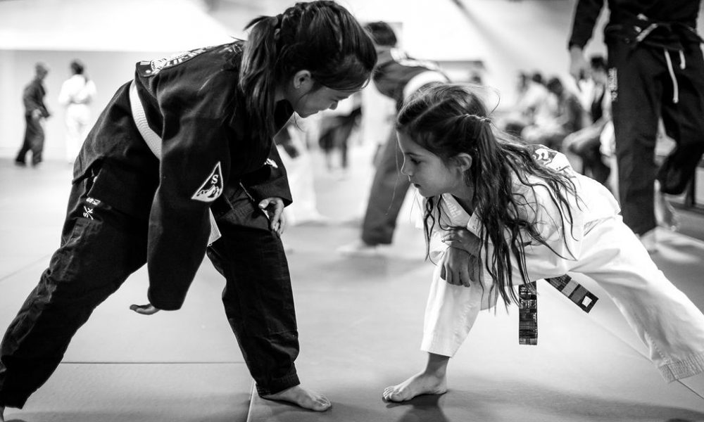 two young girls wearing Brazilian Jiu Jitsu kimonos face off, as one prepares to shoot for a takedown