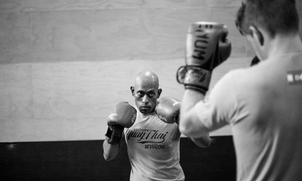 Two men wearing Easton Muay Thai shirts and boxing gloves face each other with their guards raised.