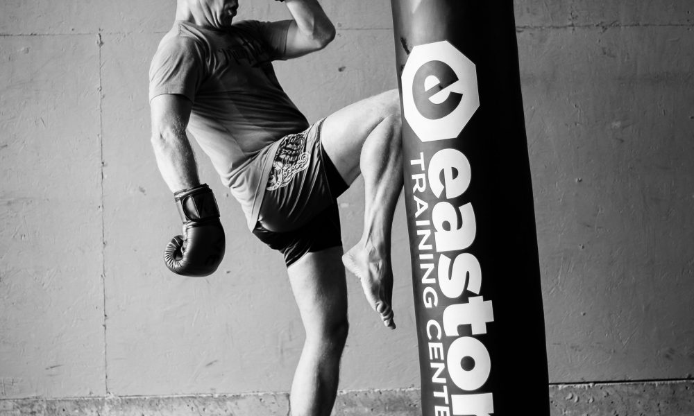 M.THURK_9450 a man knees a punching bag labeled with the words "Easton Training Center" in a kickboxing class