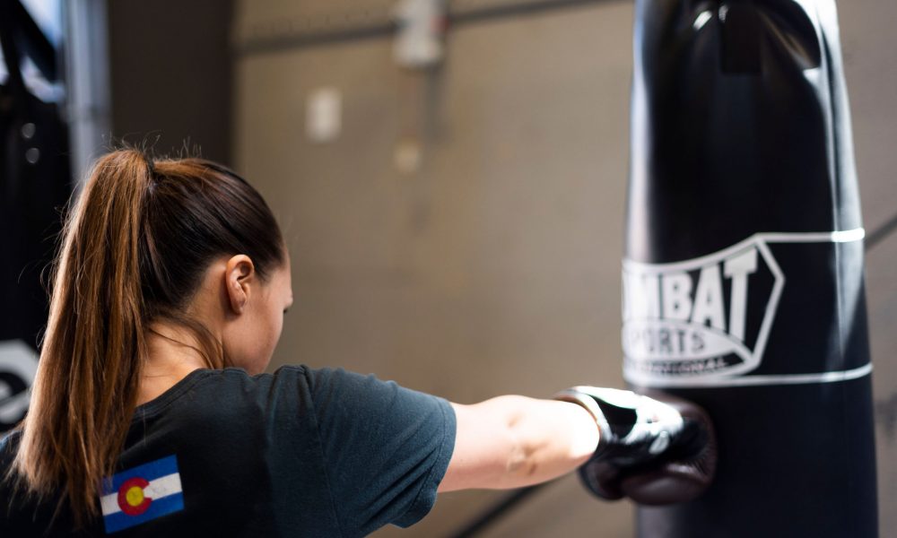 a woman wearing boxing gloves punches a heavy bag with a right cross